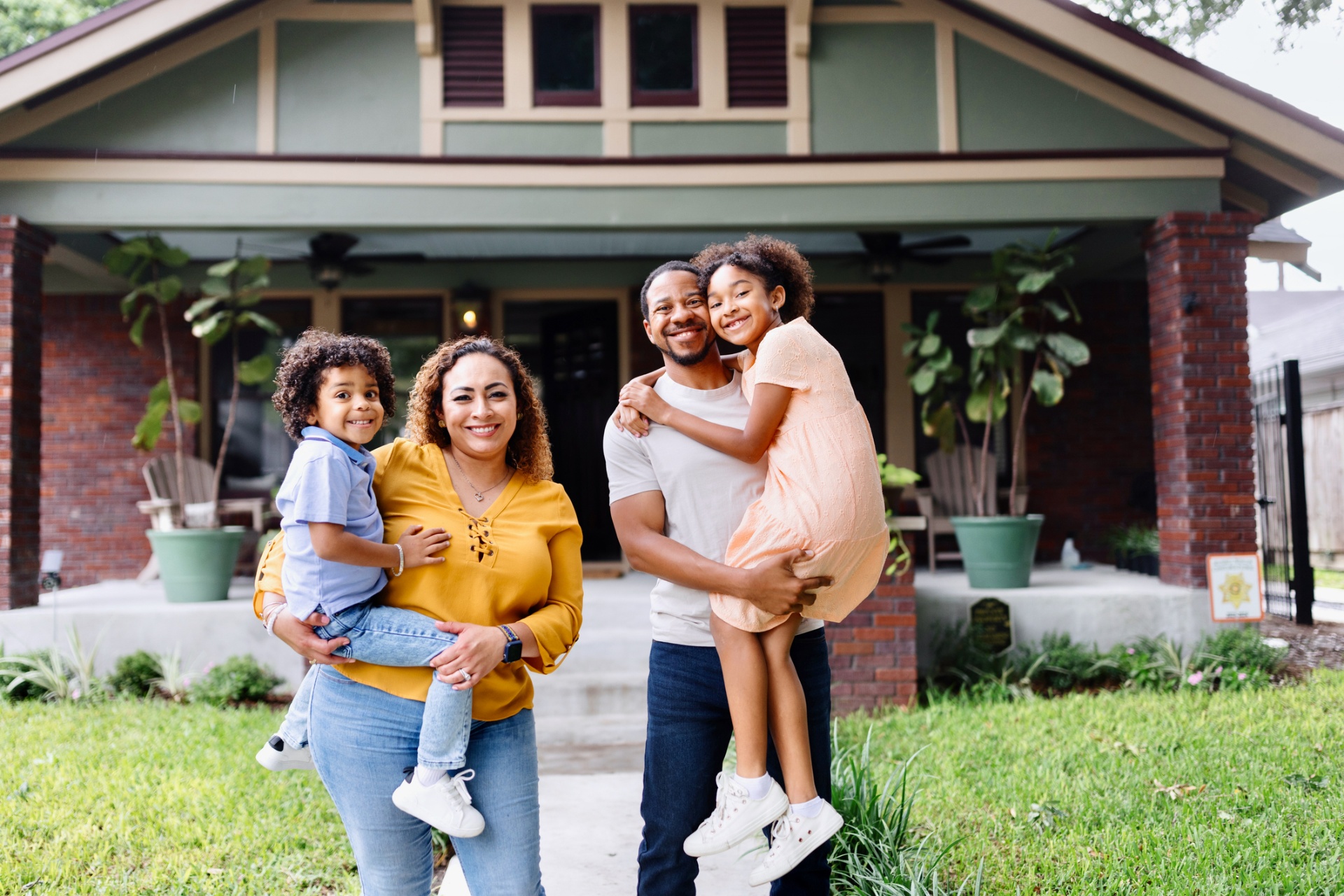 A young family standing together on the porch of their restored home